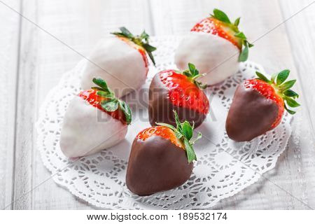Fresh strawberries dipped in dark and white chocolate on light background close up. Delicious dessert and candy bar. Top view