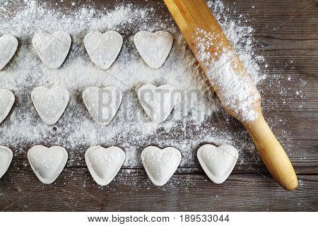 Heart shaped ravioli with flou and rolling pin on vintage wood table background. Cooking dumplings. Top view.