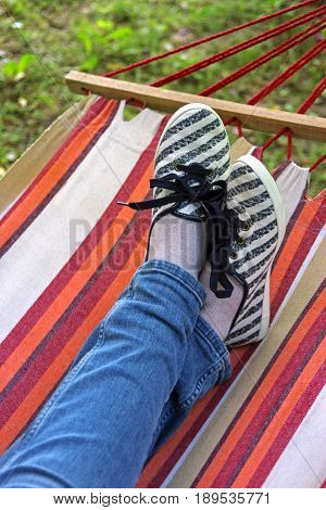 crossed legs in a colorful striped hammock wearing blue jeans and cloth shoes