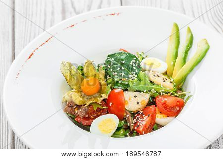 Fresh salad with tuna spinach arugula codfish artichokes quail eggs avocado cherry tomatoes physalis and sesame on wooden background close up. Mediterranean food