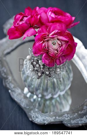 Close-up floral composition with a pink ranunculus flowers in a beautiful vase on a silver tray.