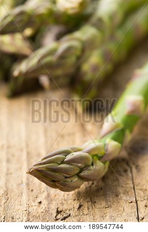 Bundle of fresh cut raw uncooked green asparagus vegetable on rustic wood table background - selective focus on tip of the bud