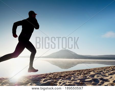 Healthy Lifestyle. Tall Young Man Runner Is Running On Sunrise Seaside. Man Jump In Sand