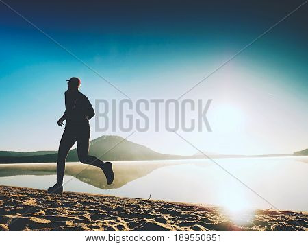 Healthy Lifestyle. Tall Young Man Runner Is Running On Sunrise Seaside. Man Jump In Sand