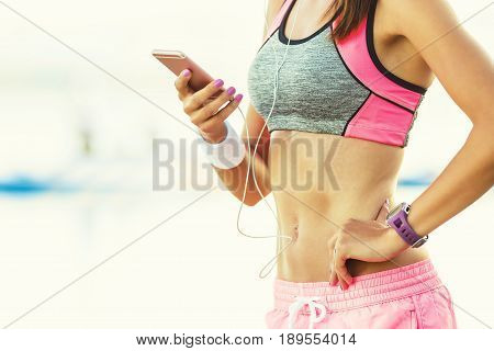 Attractive young woman on the beach after running listening to music on smartphone using earphones. Woman in sport outfit.