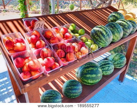 Classical road Greek stand rack shelf board table with colorful fruits peaches figs water melons for car traveling tourists on Greece Rodos island. Greece islands holidays vacation car travel tours