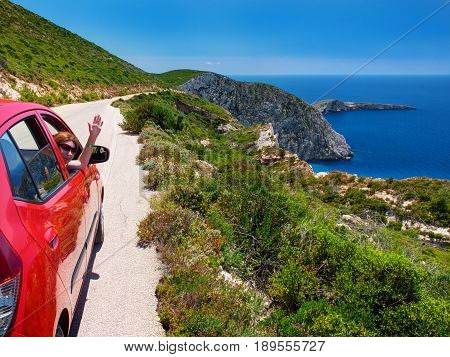 ZAKYNTHOS ISLAND, GREECE, JUN,06, 2016: Beautiful perspective view on red car on road with pretty girl, Ag. Ioannis island in Ionian Sea. Famous sightseeing car travel. Greece holidays vacations tours