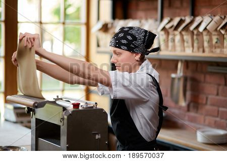 Woman working with dough and pasta rolling machine on the kitchen of restaurant. Making pasta. Making pasta in restaurant. Woman preparing knead for pasta