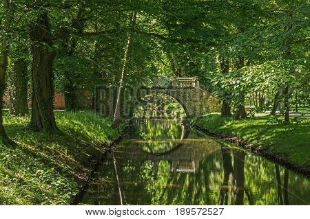 The photo shows a historic stone bridge over the small river Czerna, located in the palace and park complex located in Iłowa, in western Poland. 