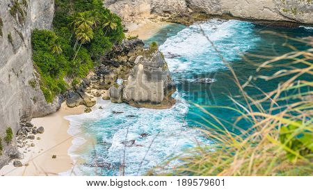 Rock in the ocean with beautiful palms behind at Atuh beach on Nusa Penida island, Indonesia.