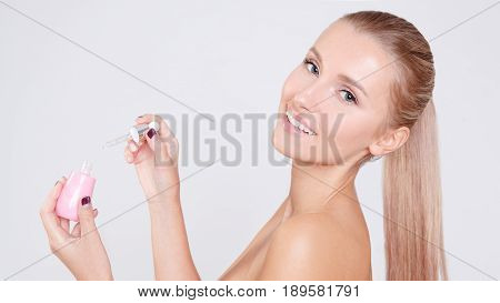 Portrait of young beautiful caucasian woman opening and applying serum isolated over grey background. Cleaning face, perfect skin. SPA therapy, skincare, cosmetology and plastic surgery concept. Studio