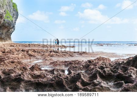 Niue, South Pacific - May 25, 2017;  Mother and son exploring rock pools in distance on coral shelf on tropical Niue