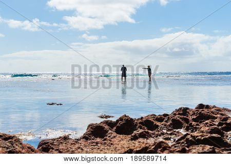 Niue, South Pacific - May 25, 2017;  Two figures silhouetted exploring rock pools on coral shelf on tropical Niue