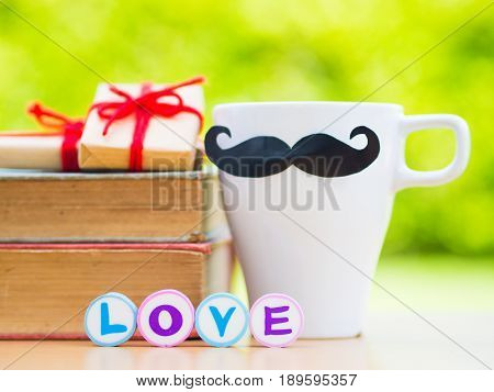 Father's day concept. LOVE DAD alphabet on stack of books gifts tea cup with black Mustache and flower on background
