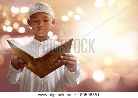 Asian muslim kid reading koran with bokeh background