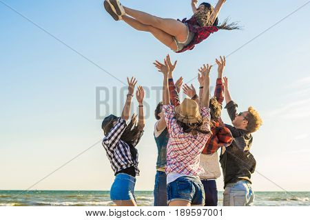 Group of hipster young friends on beach together tossing up a girl. Freedom and frienship concept