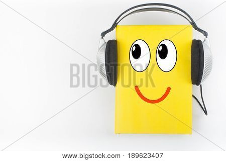 Audiobook on white background. Headphones put over yellow hardback book, empty cover, copy space for ad text. Distance education, e-learning concept