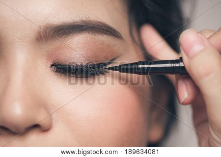 Close-up Portrait Of Beautiful Girl Touching Black Eyeliner To Her Eyelid With Closed Eyes.