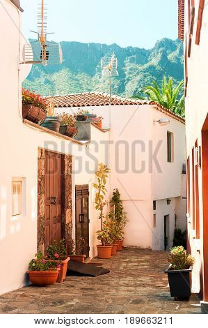 Sunny hilly street with small pink houses in rocks mountains. Spain Canary islands Tenerife Maska. Multi colored vibrant summertime utdoors vertical image.