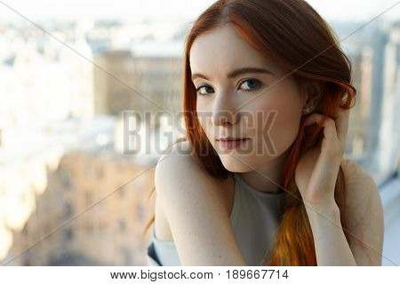 Close up portrait of pretty European appearance teenage girl looking thoughtful and dreamy at camera. Gorgeus redhead student female with colored strands of hair and green eyes on old city background