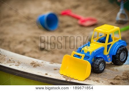 Closeup of bright blue and yellow tractor and children plastic shovel and pail in the sandbox. Baby's toys outdoor.