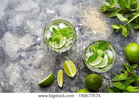 Mojito cocktail alcohol drink top view in highball glass, summer tropical vacation beverage with rum, mint leaves, lime citrus juice, soda water and ice on concrete table.