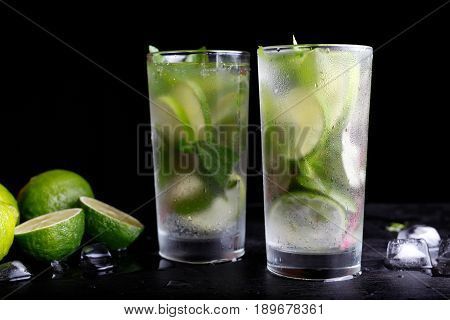 Mojito traditional summer vacation refreshing cocktail alcohol drink in highball glass, soda water beverage, lime juice, mint leaves, sugar, and rum. Dark black background with copy space text