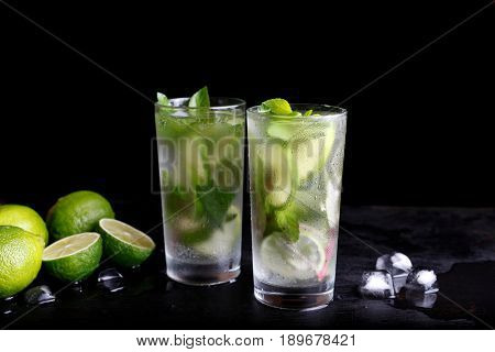 Mojito summer vacation refreshing tropical cocktail alcohol drink in highball glass, soda water beverage, lime juice, mint leaves, sugar, and rum. Dark black background with copy space text