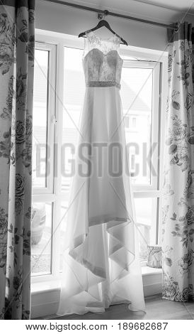 Wedding dress haning in a window taken vertically in monochrome black and white.