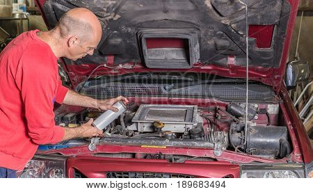 Mechanic working on a car engine he is holding a can or aerosol spray