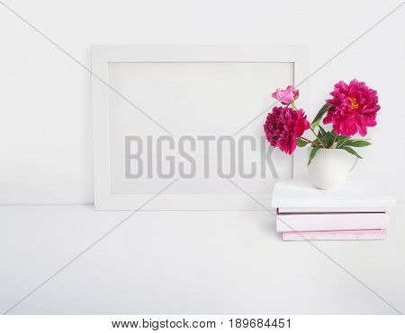 White blank wooden frame mockup with a peony flowers bouquet in a porcelain cup and pile of books lying on the table. Poster product design, styled stock feminine photography. Home decor.
