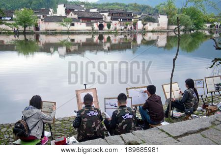 HONGCUN, CHINA - APRIL 20, 2014: Group of young artists painting landscape on canvas in ancient village in Anhui province.
