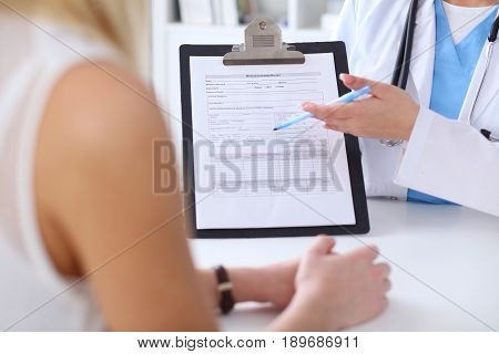 Close up of a doctor and  patient hands while phisician pointing into medical history form at clipboard. Medicine and health care concept