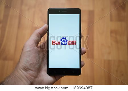 London, United Kingdom, june 5, 2017: Man holding smartphone with Baidu logo on the screen. Laminate wood background.