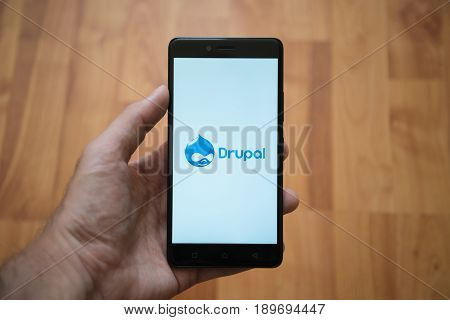 London, United Kingdom, june 5, 2017: Man holding smartphone with Drupal logo on the screen. Laminate wood background.