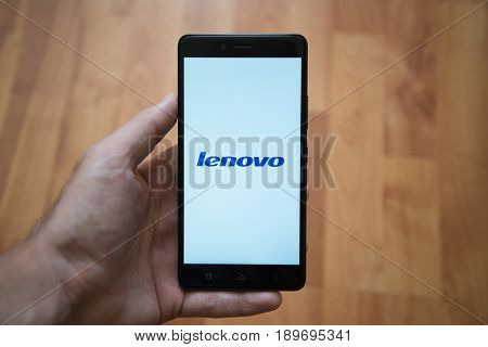 London, United Kingdom, june 5, 2017: Man holding smartphone with Lenovo logo on the screen. Laminate wood background.
