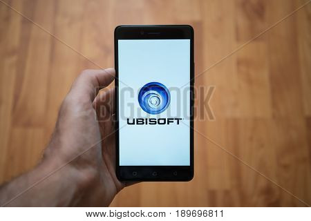 London, United Kingdom, june 5, 2017: Man holding smartphone with Ubisoft LOGO on the screen. Laminate wood background.