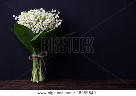Lily of the valley on dark wooden background. Lily of the valley bouquet. Space for text.