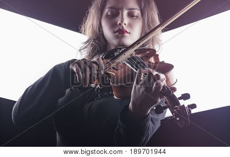 Beautiful young woman playing the violin on dark background