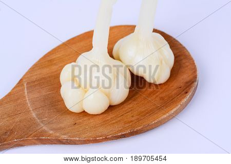 Pickled garlics on a wooden spatula.  White background.