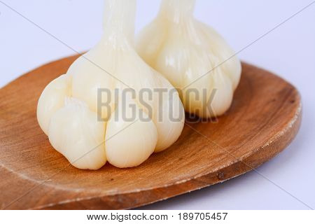 Close up of pickled garlics on a wooden spatula.  White background.