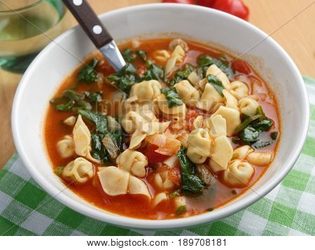 Tomato tortellini spinach soup on a rustic table