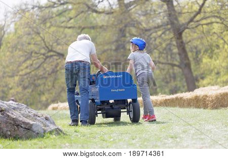 STOCKHOLM SWEDEN - MAY 21 2017: Rear view of granpa and grandchild push a soapbox car up the hill in the race Gardesloppet at Djurgarden Stockholm Sweden. May 21 2017