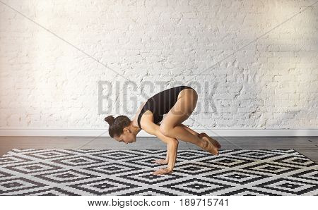 Young asian woman in the Bakasana Crane yoga pose. Attractive female practicing handstand asana for the development of balance, harmony, concentration and health in modern fit hall. Yoga concept