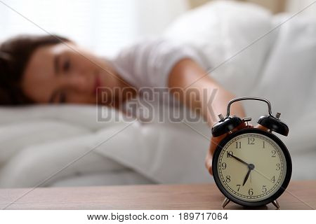 Sleepy young woman stretching hand to ringing alarm willing turn it off. Early wake up, not getting enough sleep, getting work concept.