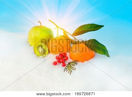 Christmas fruit in snow - orange green apple red berries viburnum kiwi in snow before Christmas in sunny winter afternoon against the blue sky