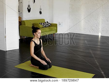 Asian young Businesswoman practicing Vajrasana before hard day sitting on her feet knees on a green yoga mat. Calmness and relax woman happiness. Yoga and health concept. Copy space for your content