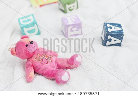 A cute pink bear soft toy with I Love You words written on the bear.  Cubes of alphabet around the soft toy.  White background.