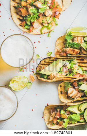 Healthy corn tortillas with grilled chicken fillet, avocado, fresh salsa, limes, beer over light grey marble background, top view. Healthy food, gluten-free, weight loss, allergy-friendly concept