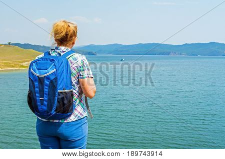 Woman backpacker on the shore of Lake Baikal. Olkhon Gates Strait. In the distance - Olkhon island
